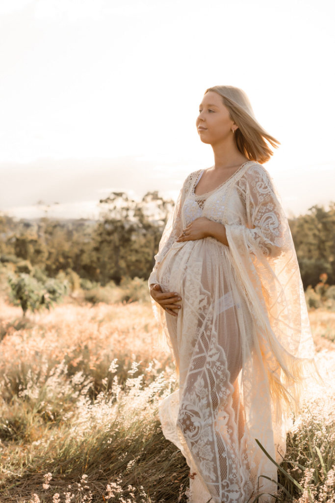 Pregnant Mama in sheer lace dress walking in a grassy field. A Golden Hour Shoot
