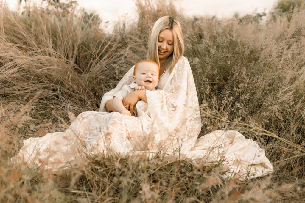 Pregnant Mama in sheer lace dress holding her toddler in a grassy field. A Golden Hour Shoot