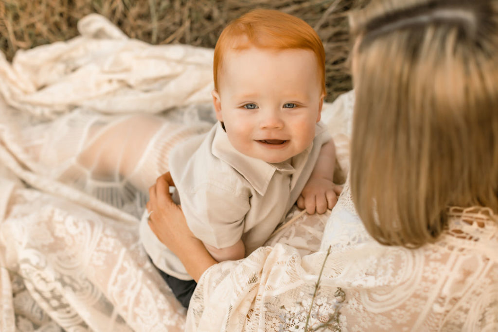 Cute boy toddler with red hair looking at the camera while sitting in his mamas lap. A Sunset shoot