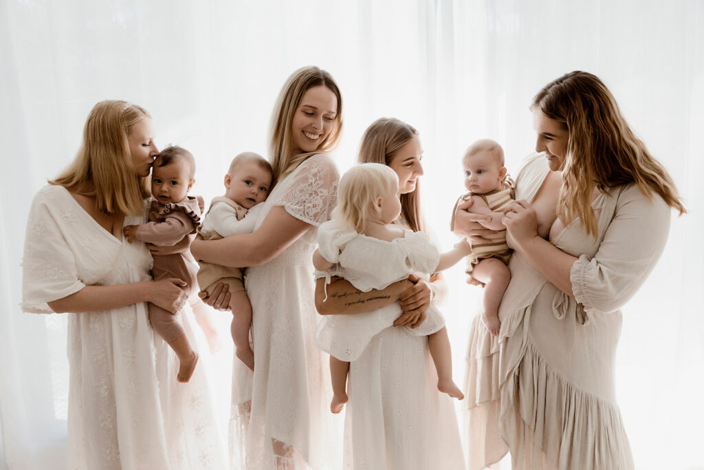 This image shows four mums standing while they hold their four bubs. All looking at the bubs.