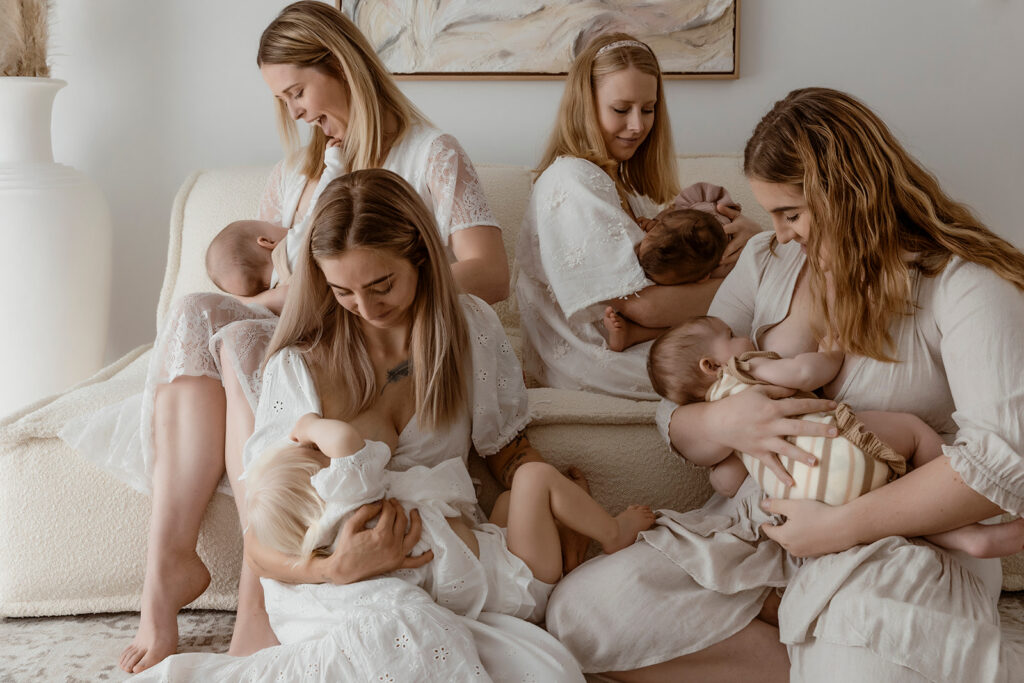 A studio shoot of four mums sitting together while they breastfeed their four bubs. All looking at the bubs.