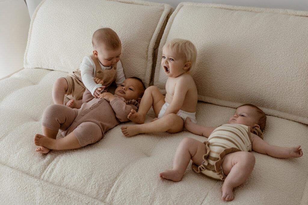 four babies on the photographers studio couch. two sitting up two laying down. 
