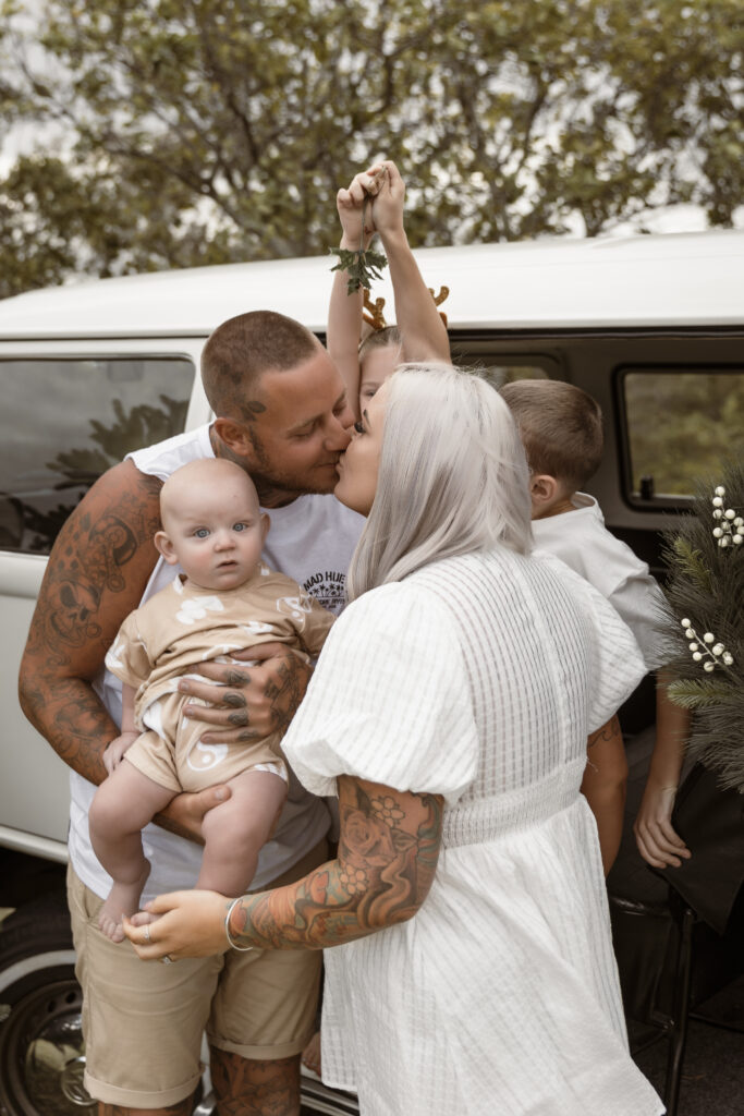 Mum and Dad kissing under the mistletoe next to a Kombi Van in an outdoor session