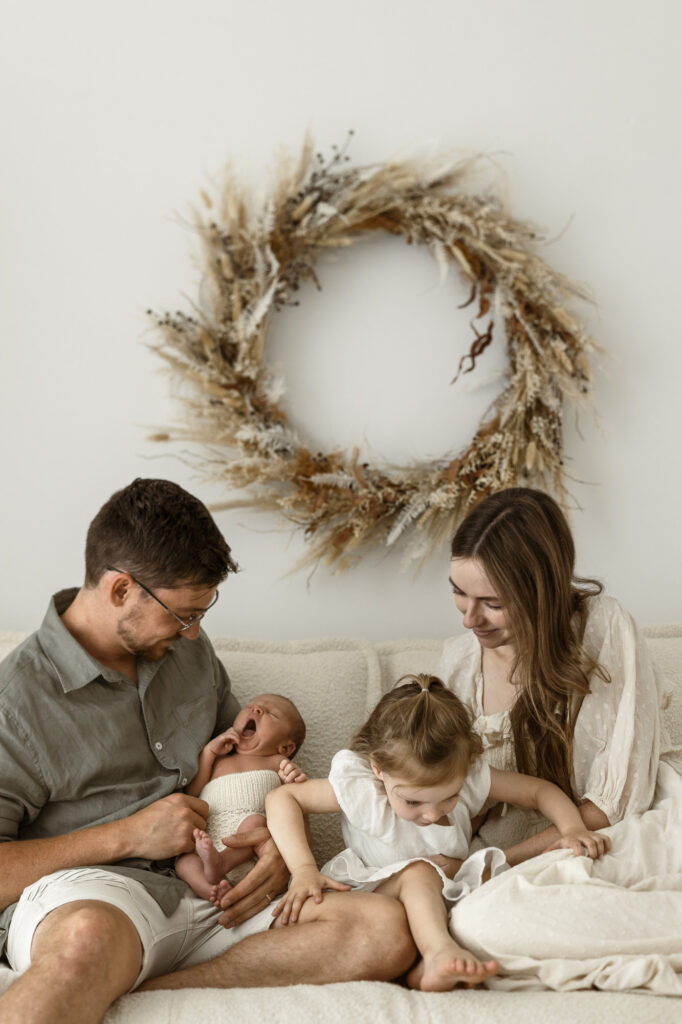 A family of four lounging on a white couch with a dried plant wreath behind them