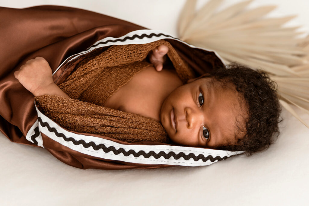 Baby laying in cultural wrap with a cultural plant behind him. Landscape view.