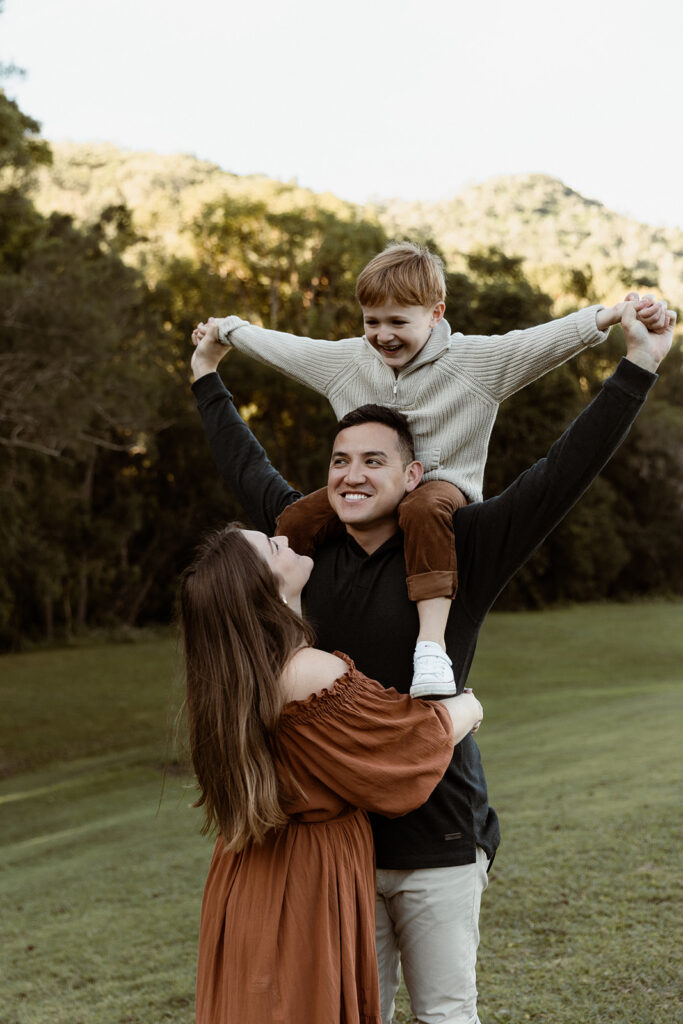 Son on dads shoulders, mum looking up at him.