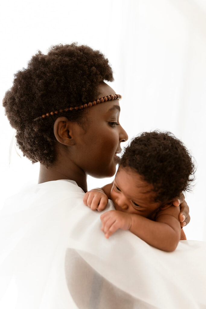 Mum holding bub, while facing away from the camera, with bub over her shoulder. She is wearing cultural attire.