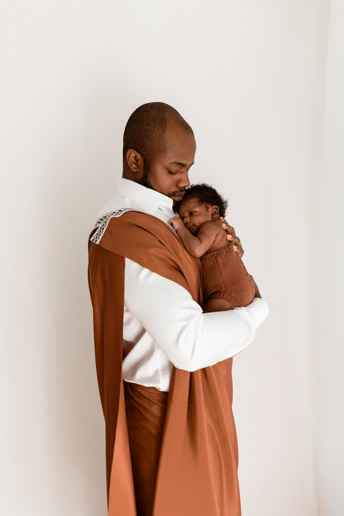 Dad holding bub, while looking down at him. Dad and bub are wearing cultural attire.